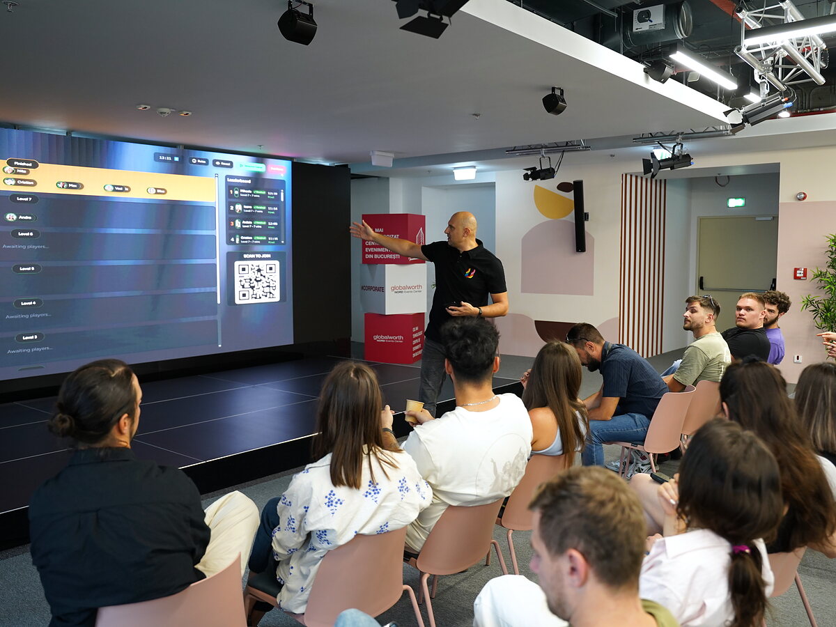 A facilitator displays the LinkO game next to the main screen and the event’s QR code.