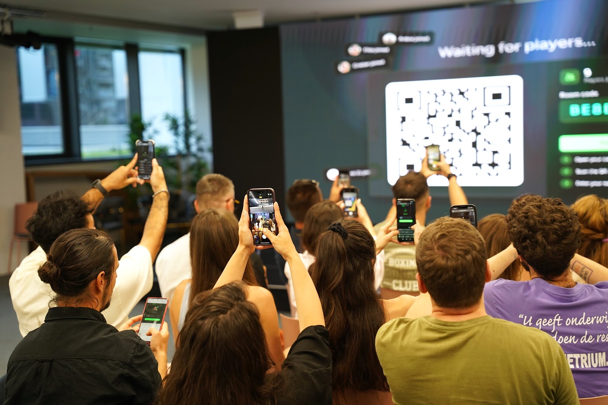 Participanți la eveniment ridică telefoanele pentru a intra în jocul interactiv LinkO prin codul QR de pe ecran.