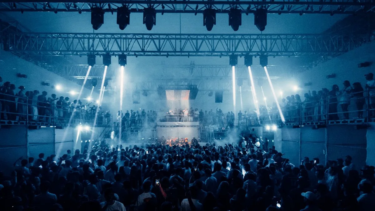 Crowd surrounding a central performance area under blue stage lighting